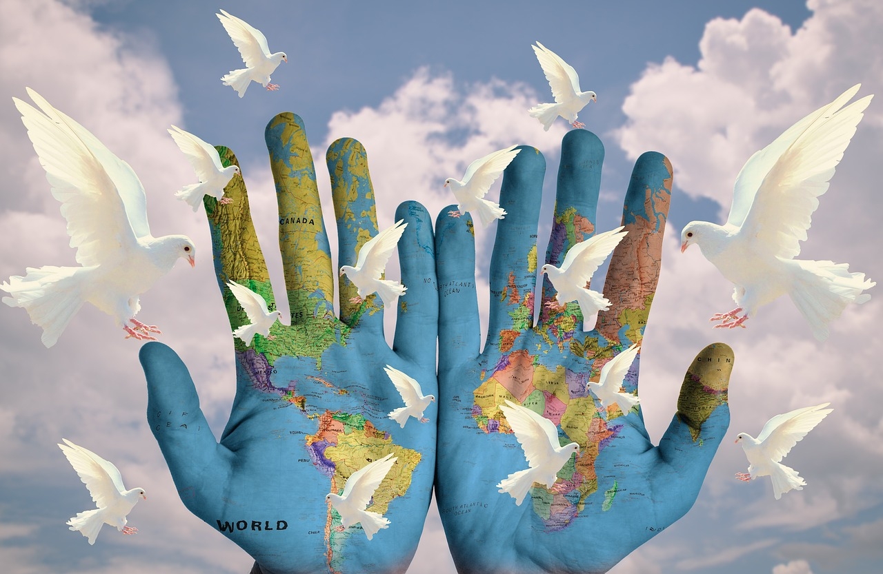 Duas mãos pintadas com o mapa mundial do planeta terra e uma pombra branca.